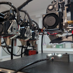 CXC tool with LEDs lit on the bed of a tool-changing 3D printer below the active toolhead